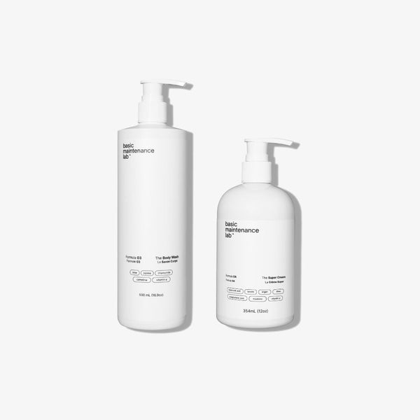 Two white pump bottles from Basic Maintenances Blemish-Free Body System are shown on a plain white background. The taller bottle is labeled The Body Wash, and the shorter one is labeled The Body Cream, both with minimalist labels.