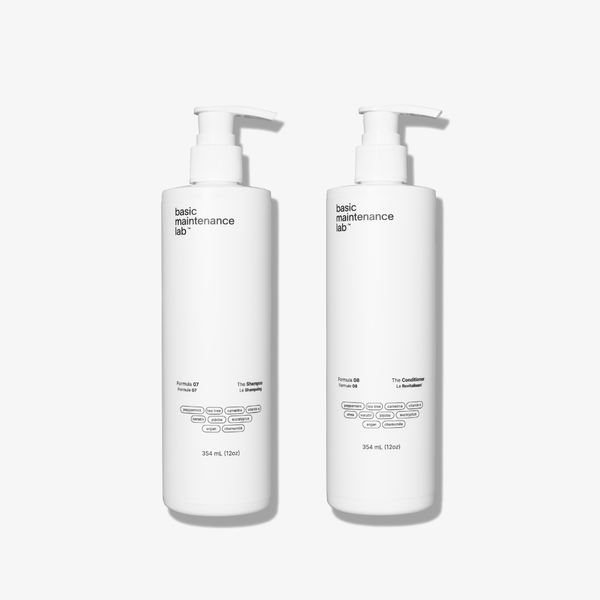 Two white pump bottles from Basic Maintenance’s Head-Turning Hair System stand side by side on a plain white background, each with minimalist black text and 354 mL size—one is The Shampoo, the other The Conditioner.