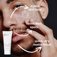 Close-up of a man applying Face + Hair Rescue Team by Basic Maintenance, with text and arrows highlighting the benefits: evens skin tone, fades dark spots, and quick-dry matte finish. The product tube appears in the corner.