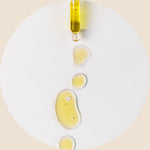 A dropper dispensing yellow oil, with several drops and pools of oil on a white surface below.