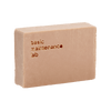 A rectangular, beige bar of The Cleansing Clay by Basic Maintenance, with the brand name engraved on one side, displayed against a transparent background.