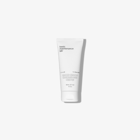 A white tube of The Face Lotion by Basic Maintenance stands upright on a plain white background, featuring minimalist black text and a simple, clean design.