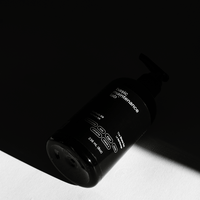 A black pump bottle of The Shave Gel by Basic Maintenance rests on a white surface, its minimalist white text and sleek design highlighted by the light while part of the bottle remains in shadow.